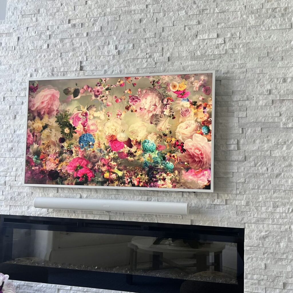 Samsung Frame TV in gallery mode with custom frame, mounted on white stone accent wall in modern smart living room.Samsung Frame TV installation with custom bezel and Control4 integration